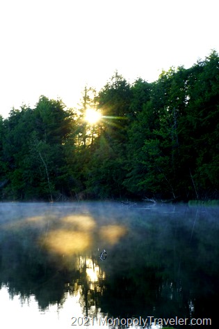 Sun rising over the calm lake with a light fog floating across